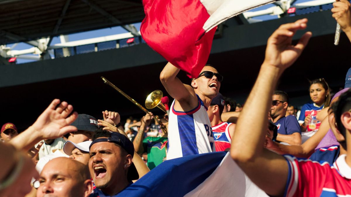 A lively group of soccer fans celebrating energetically with flags and cheering in a stadium.