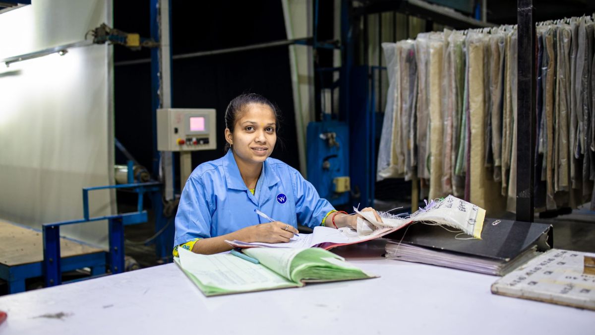 Female textile worker in factory reviewing documents at a desk.