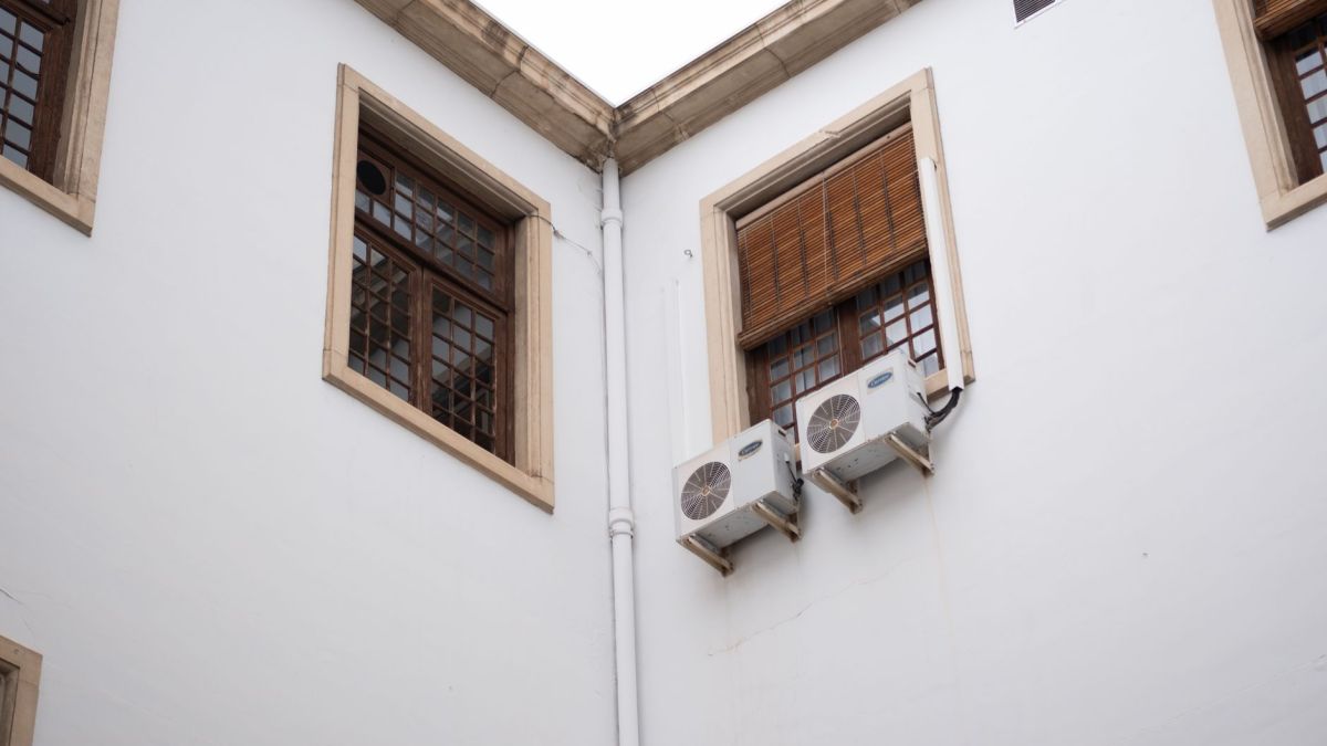 White building facade with wooden window shades and air conditioning units.