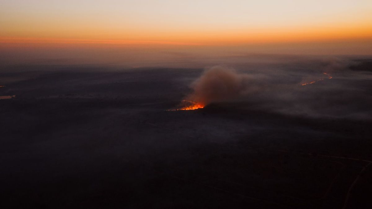 A dramatic aerial shot of a wildfire with smoke rising against a sunset backdrop in South Africa.