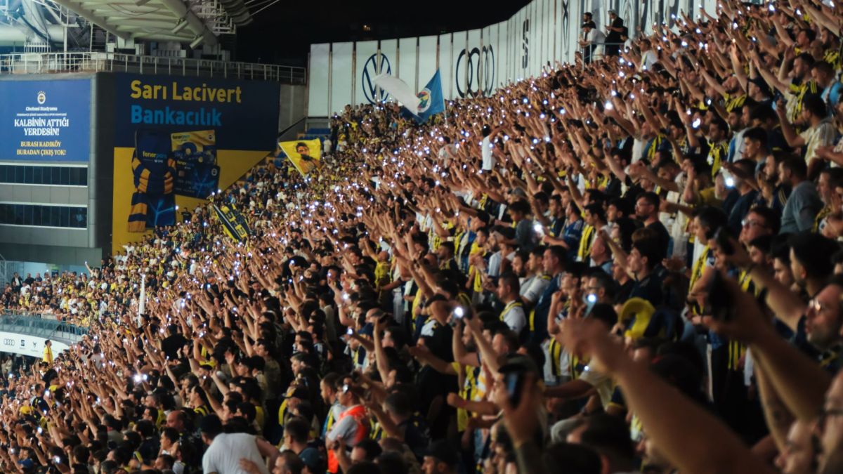 A lively crowd at a football stadium at night, showing unity and excitement with mobile flashlights.