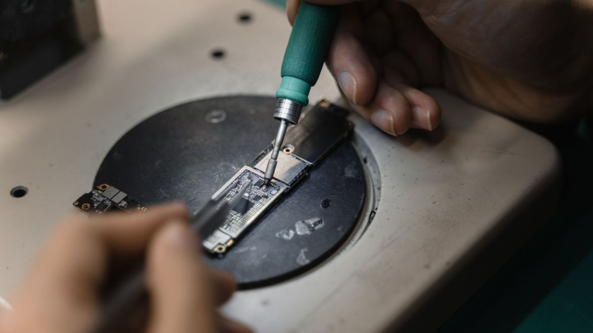 Hands using a soldering iron on circuit board, showcasing precise electronic repair indoors.