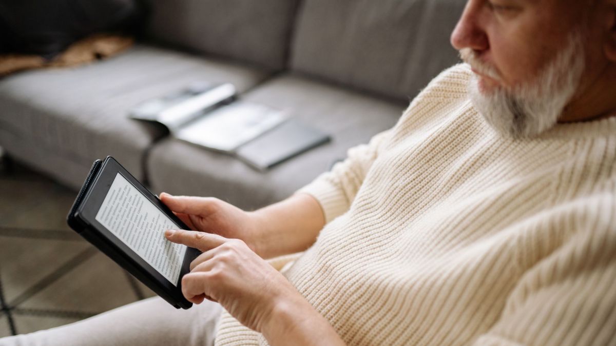 Elderly man using a tablet for reading in a cozy living room setting.